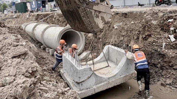 Công nhân đưa đế bê tông vào vị trí định sẵn trước khi đặt ống cống lên trên. Ảnh: Hải Lê