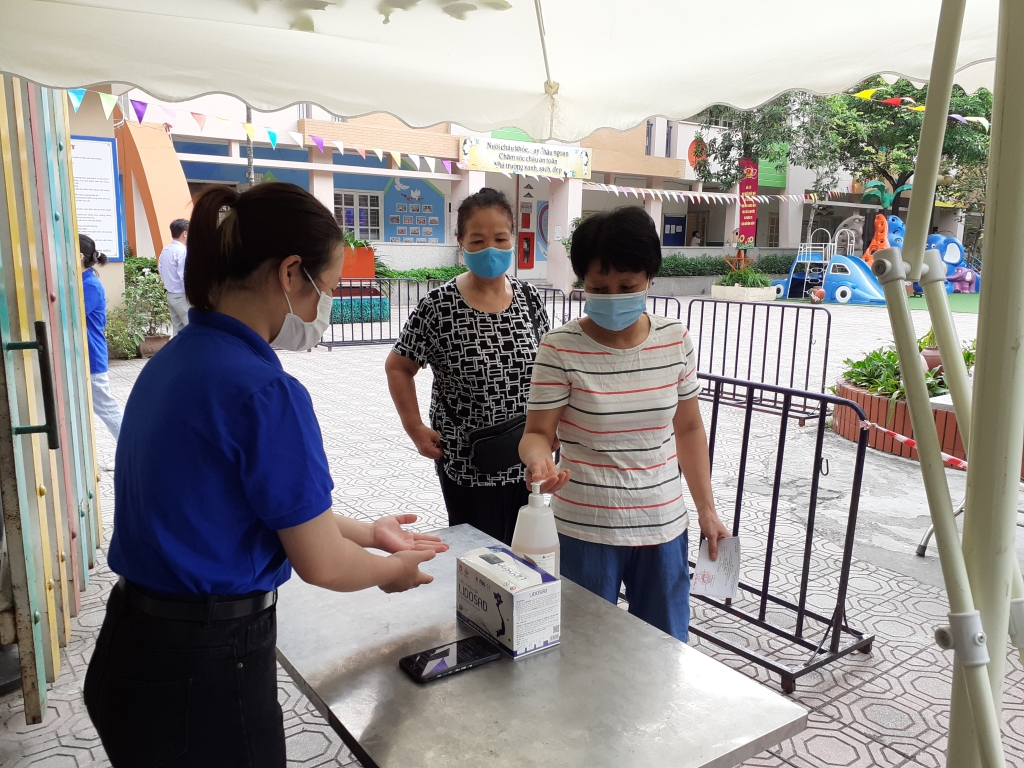 Người dân đeo khẩu trang, sát khuẩn trước khi vào trong khu vực bầu cử
